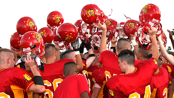 Football players raising their helmets in unity before a game.